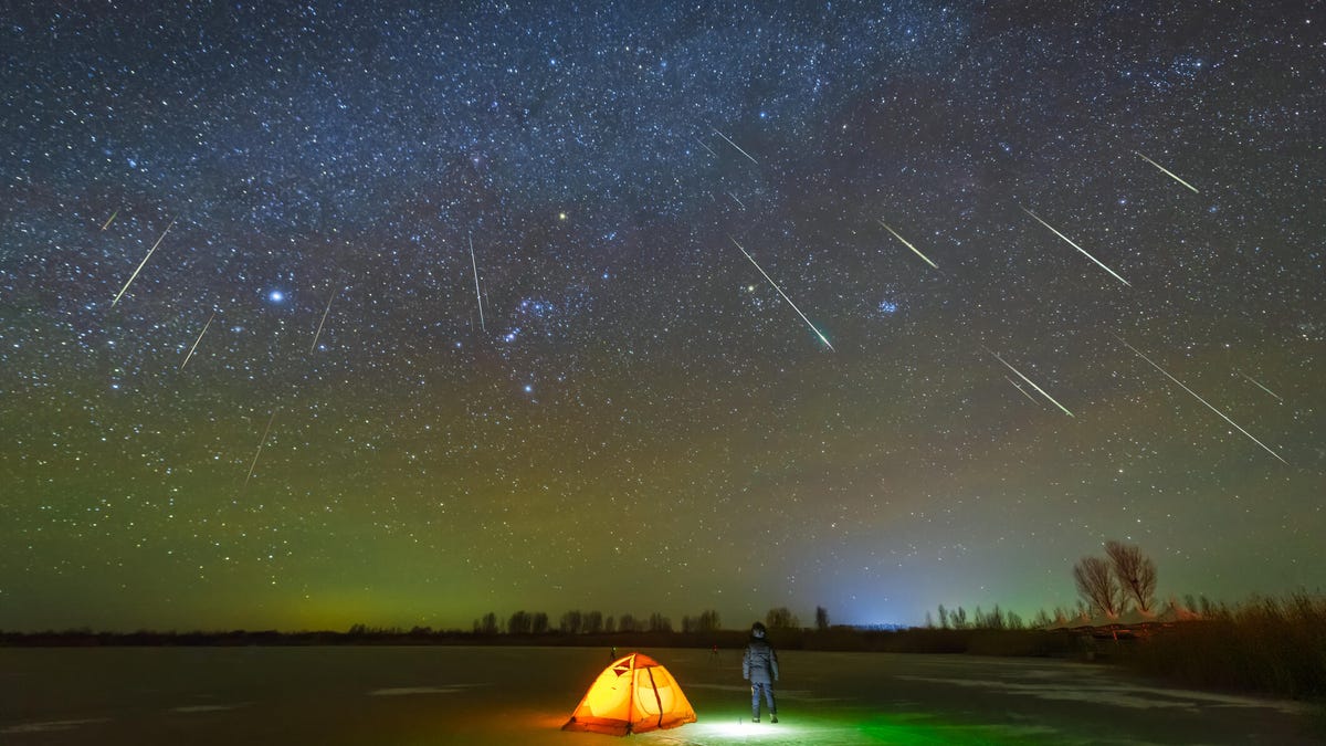 A photo of someone watching a meteor shower in a remote area, with a tent set up (gettyimages-1293344970)