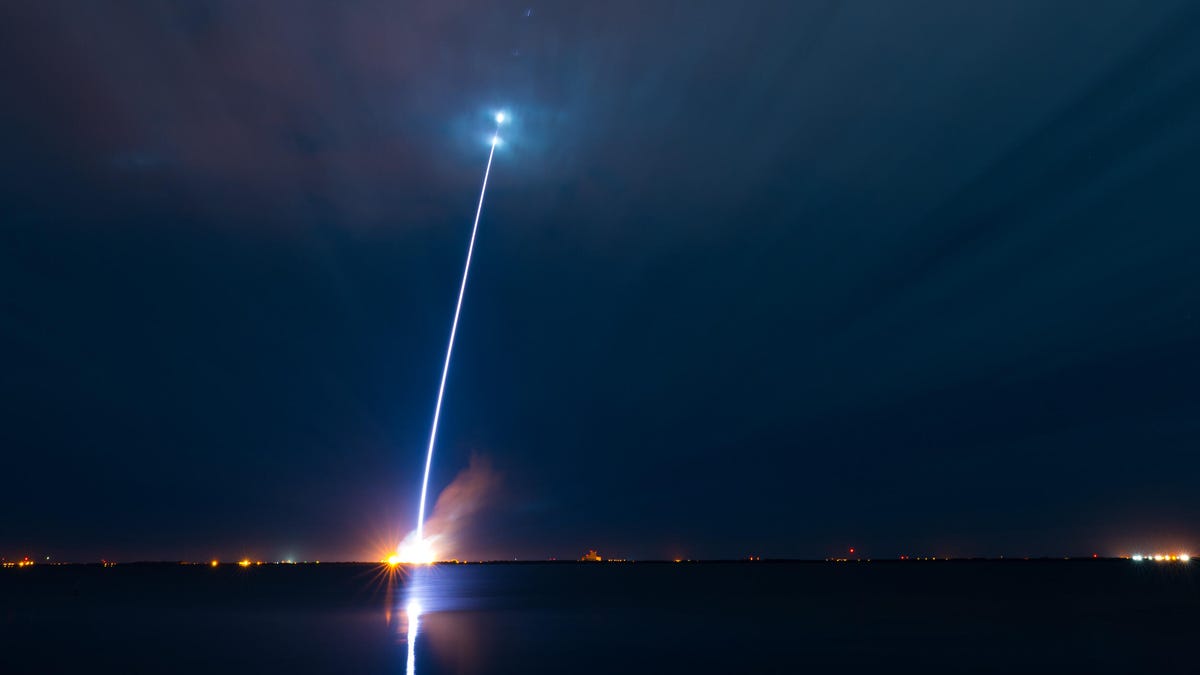 Seen from a distance, a rocket streaks into the night sky.