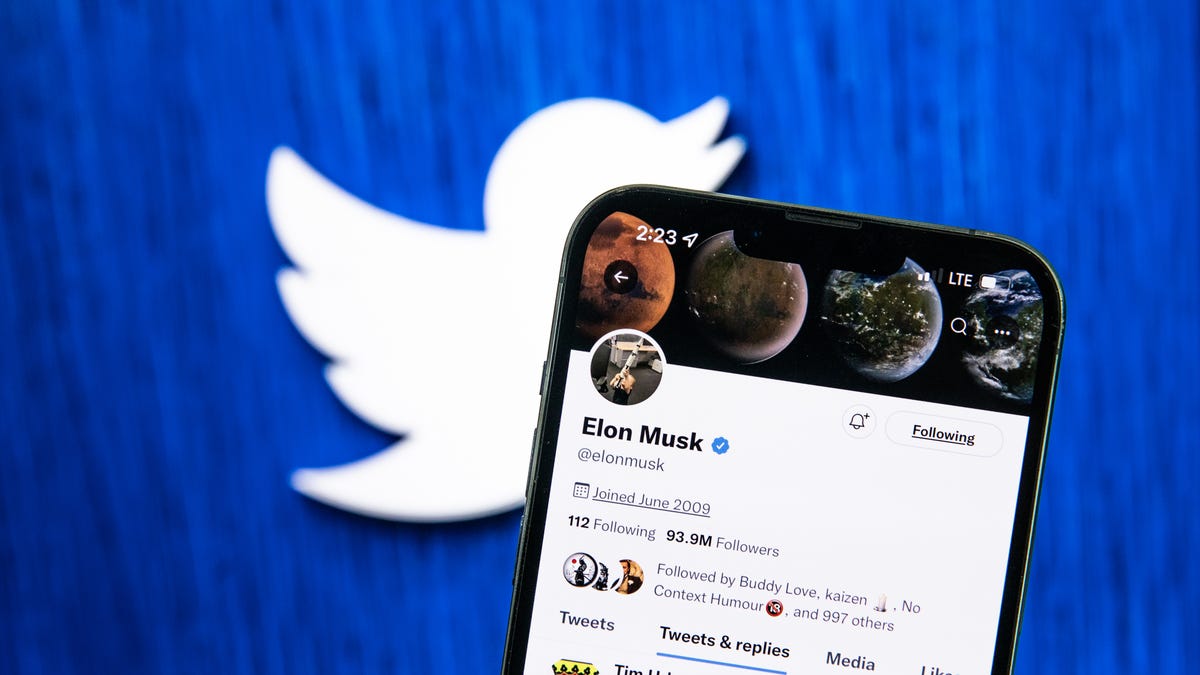 Elon Musk's Twitter account on a mobile phone, in front of a Twitter logo