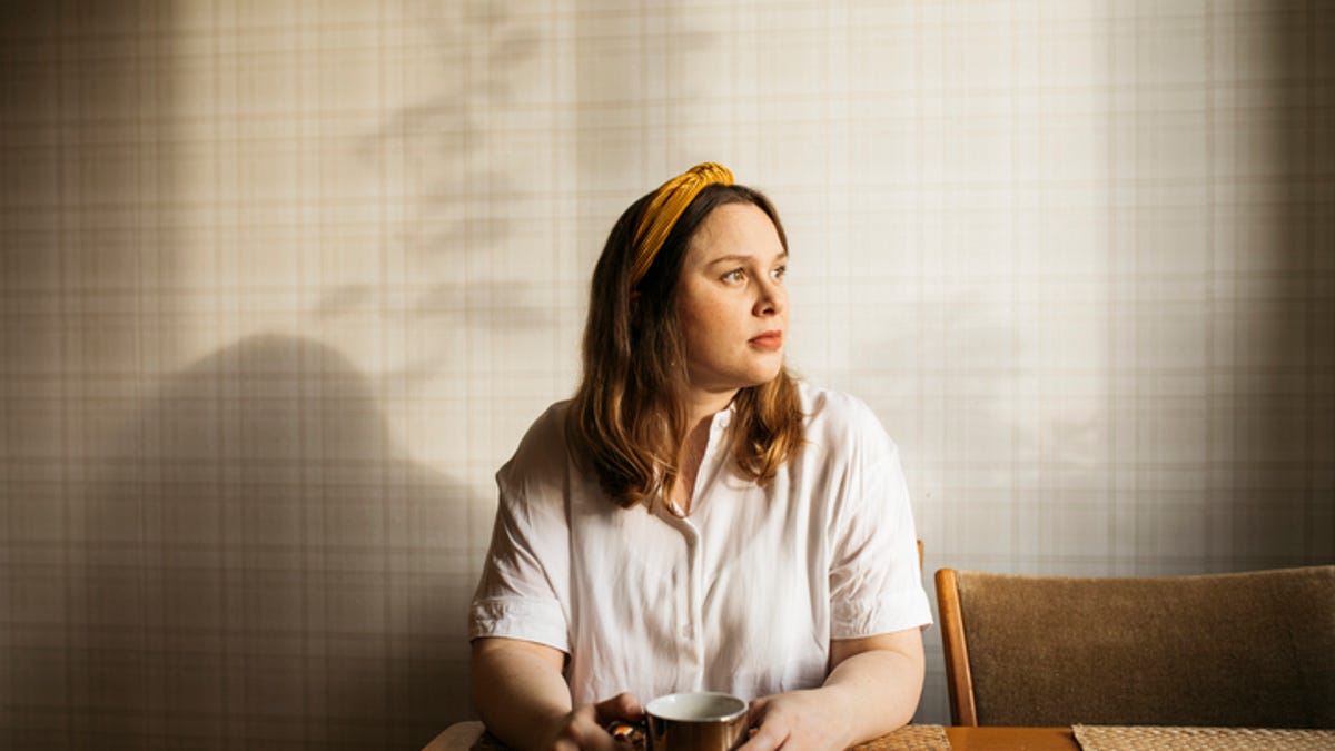 Woman sitting at a table with a mug in her hand, staring out of the window.