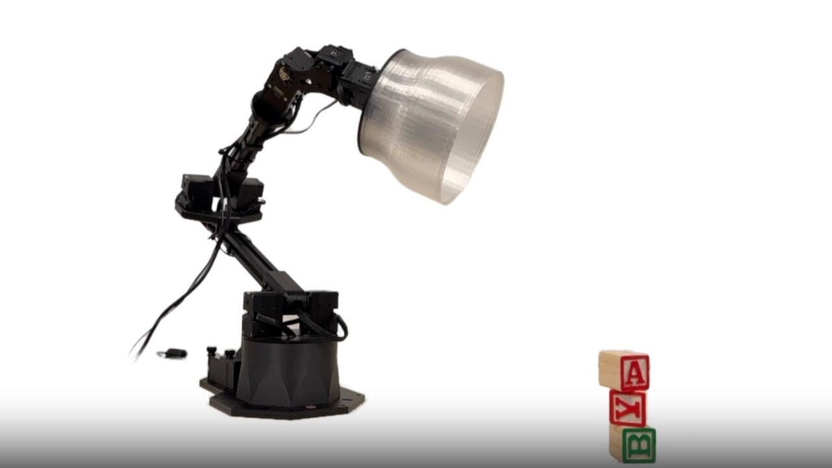 A jointed black desk lamp robot turns its shade toward a stack of wood ABC blocks.