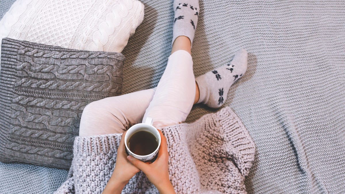 Woman sitting on a bed holding a cup of coffee in the wintertime