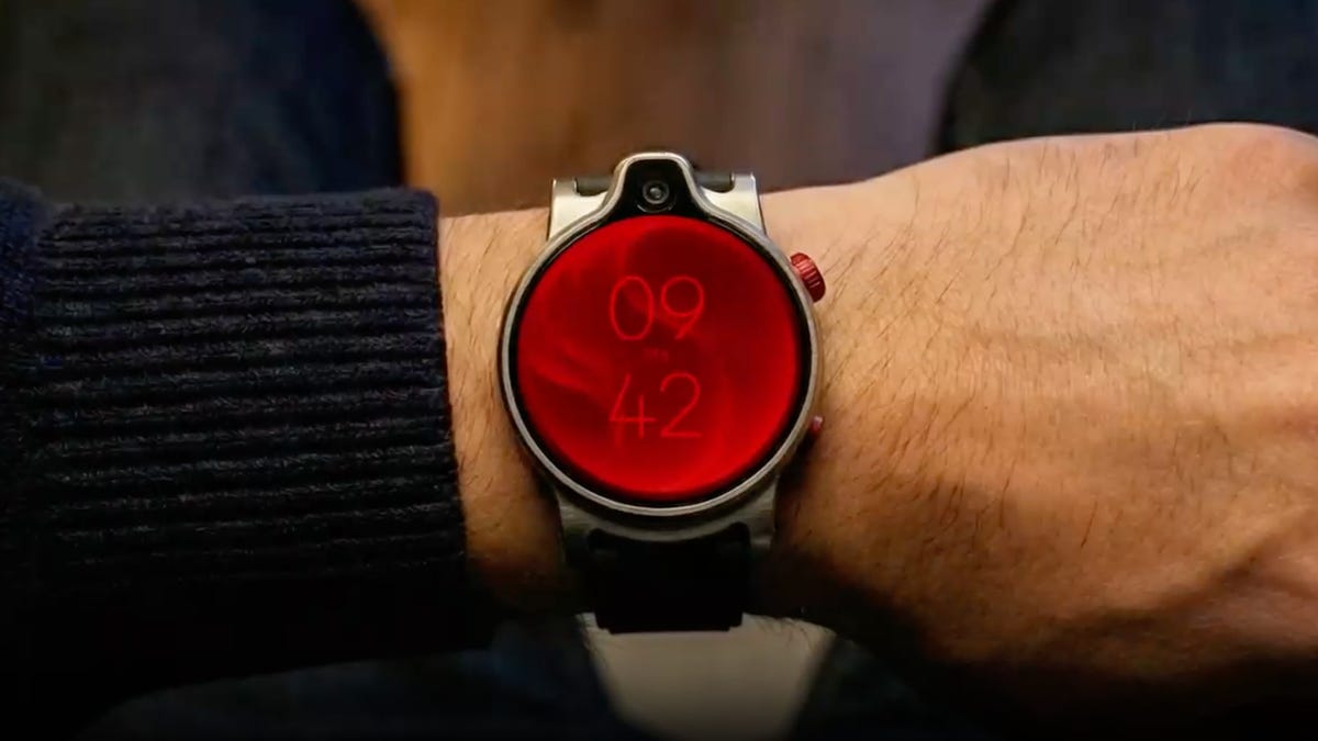 A camera-equipped prototype watch shown off by Qualcomm is being worn on a wrist. The face of the watch is red.