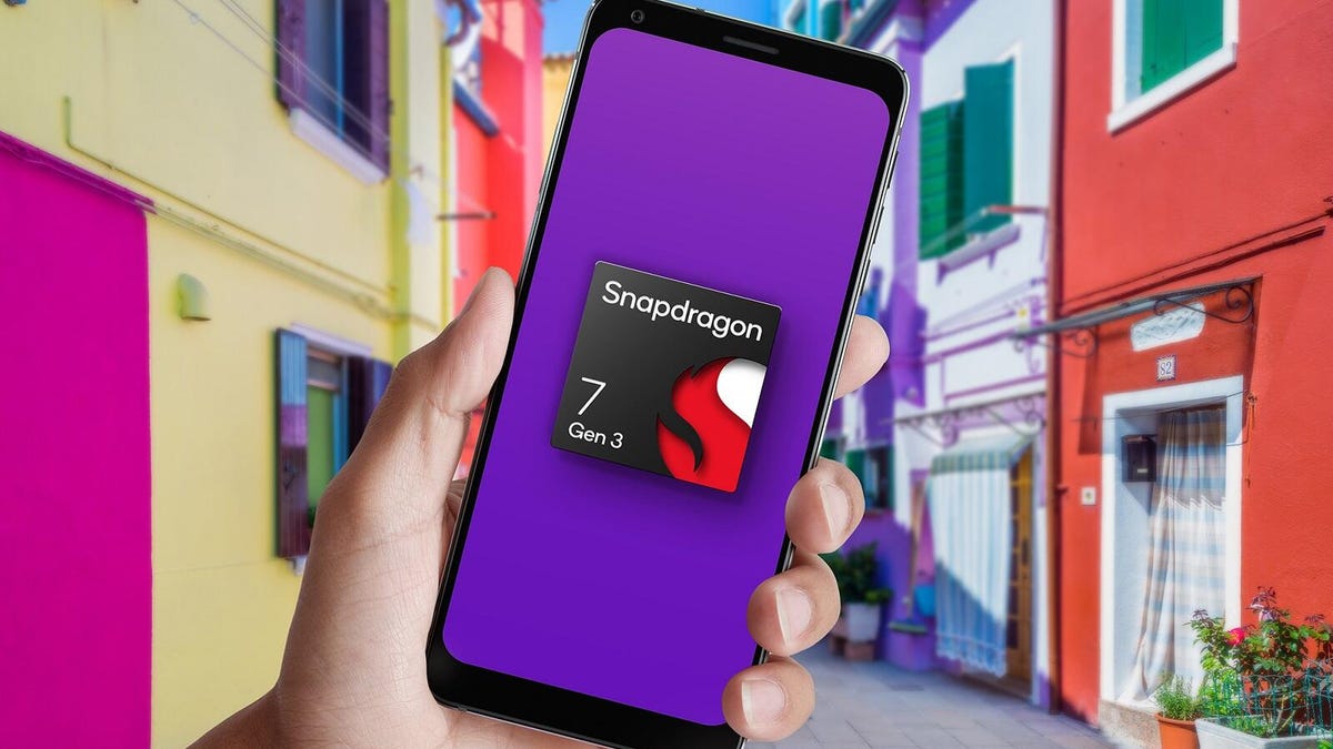 A hand holds a phone with an image of a chip labeled Snapdragon 7 Gen 3, in front of a background of colorful apartments.