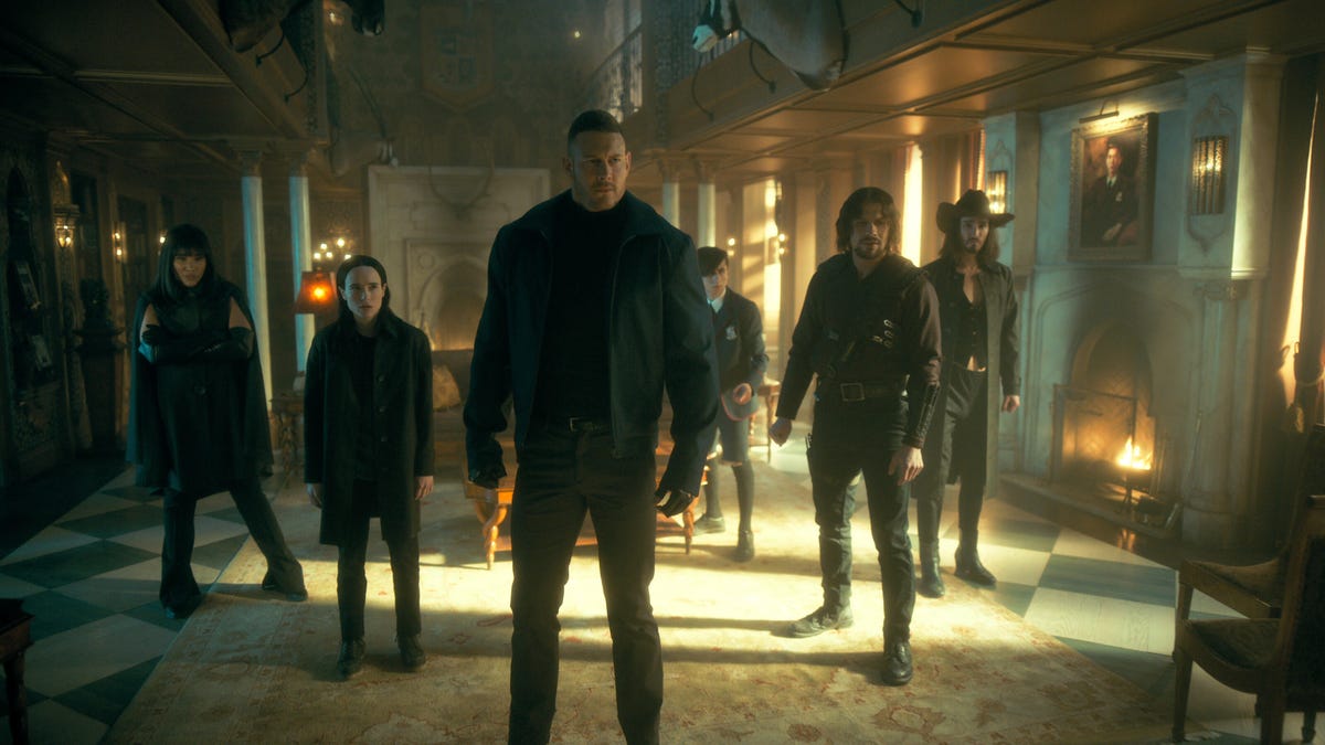 The Hargreeves siblings all standing inside their manor, dressed in black.