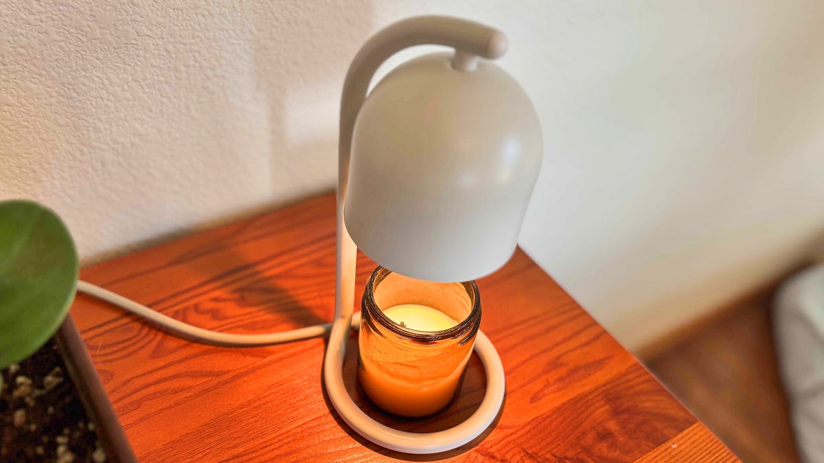 SwitchBot's candle warmer on a wood table, light with a candle.