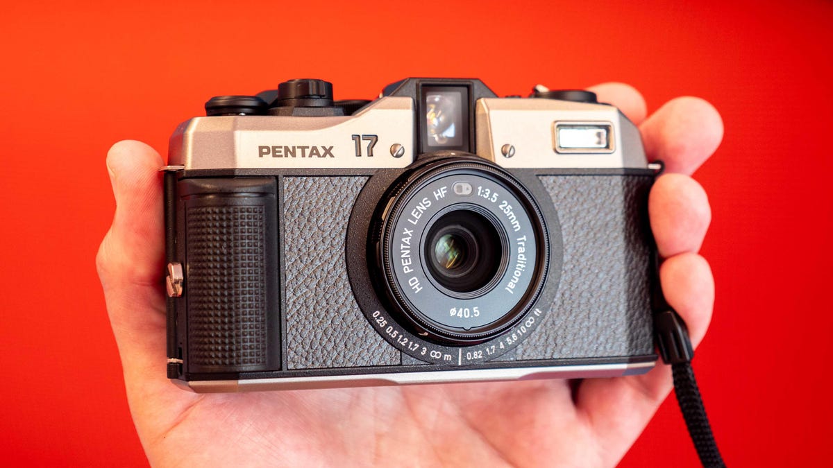 Pentax 17 compact 35mm film camera in a hand in front of a red background.