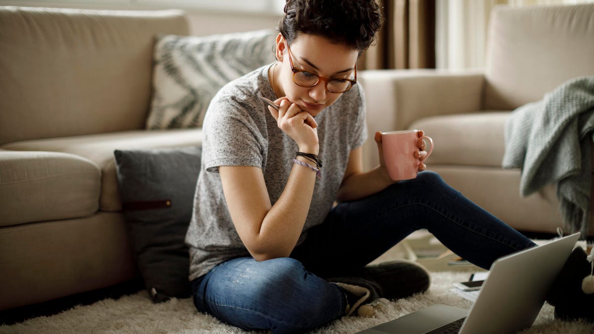 A woman sits on the floor with her laptop open and loan papers scattered around her