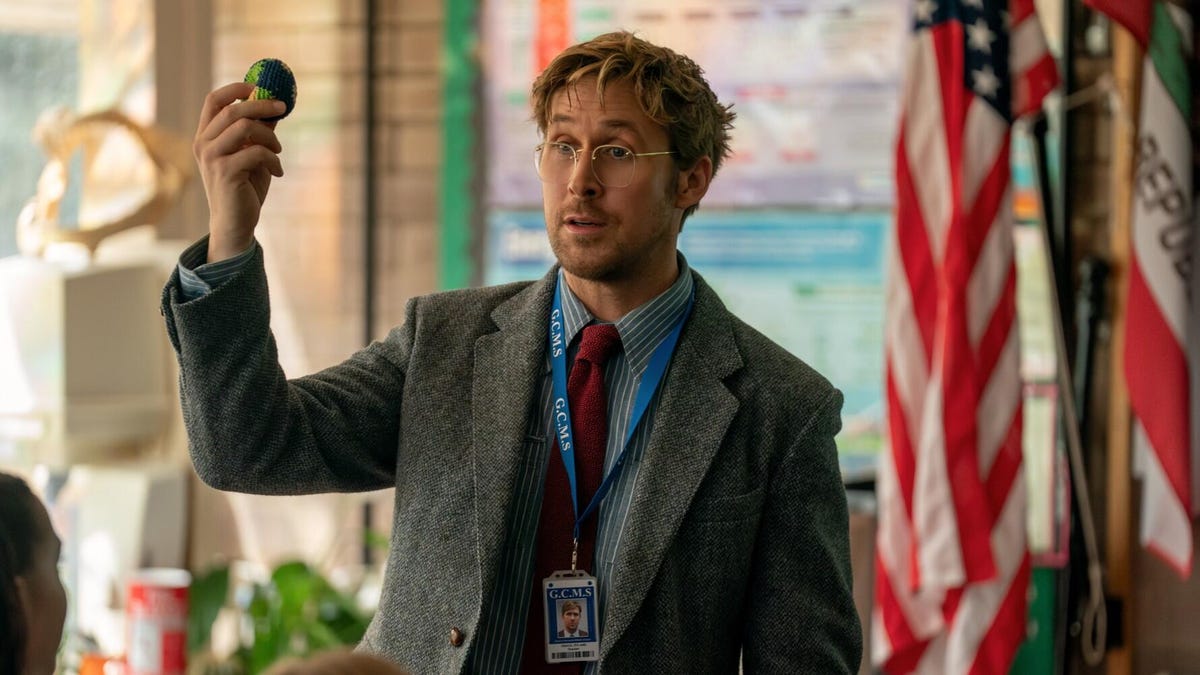 Production still from Project Hail Mary showing Ryan Gosling in a suit and glasses in a classroom holding up a mini Earth.