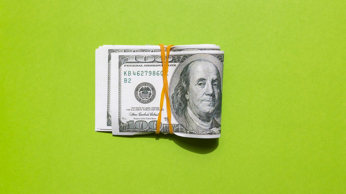 A wad of $100 bills banded off with an orange rubber band, on a lime-green background.