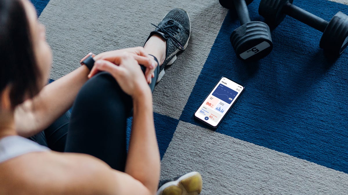 A person on the floor with weights looking down at their phone, which has workout tracking information on it.