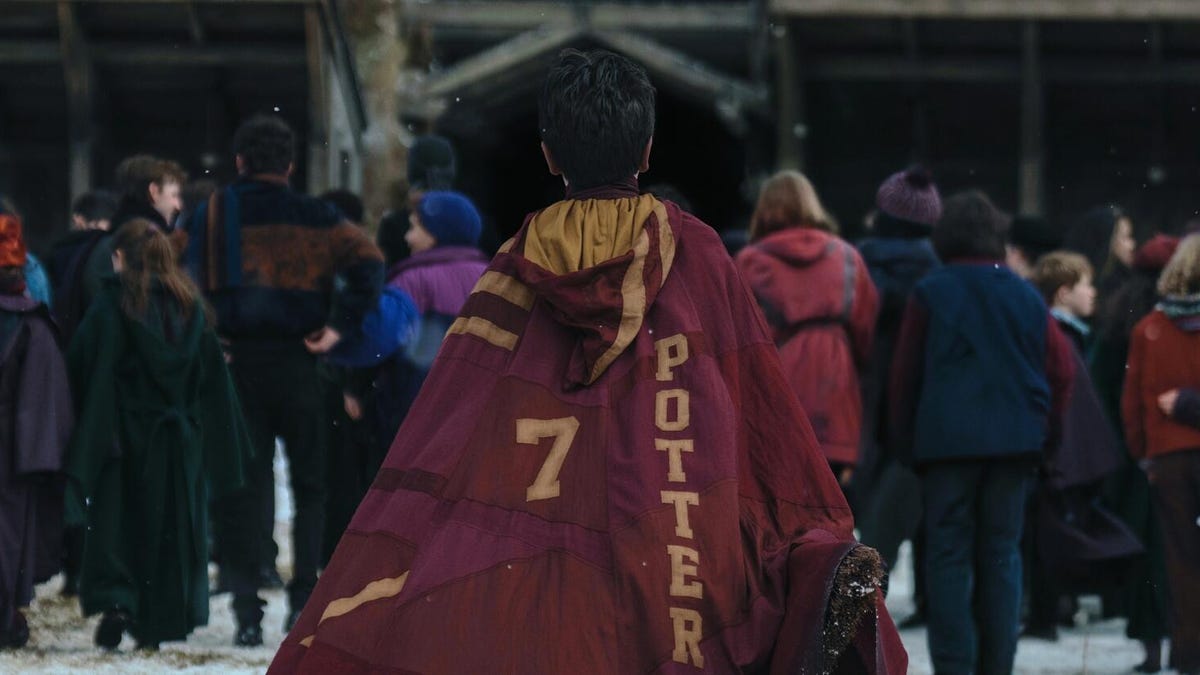 boy walks toward school wearing red and gold harry potter cape in HBO's harry potter tv series