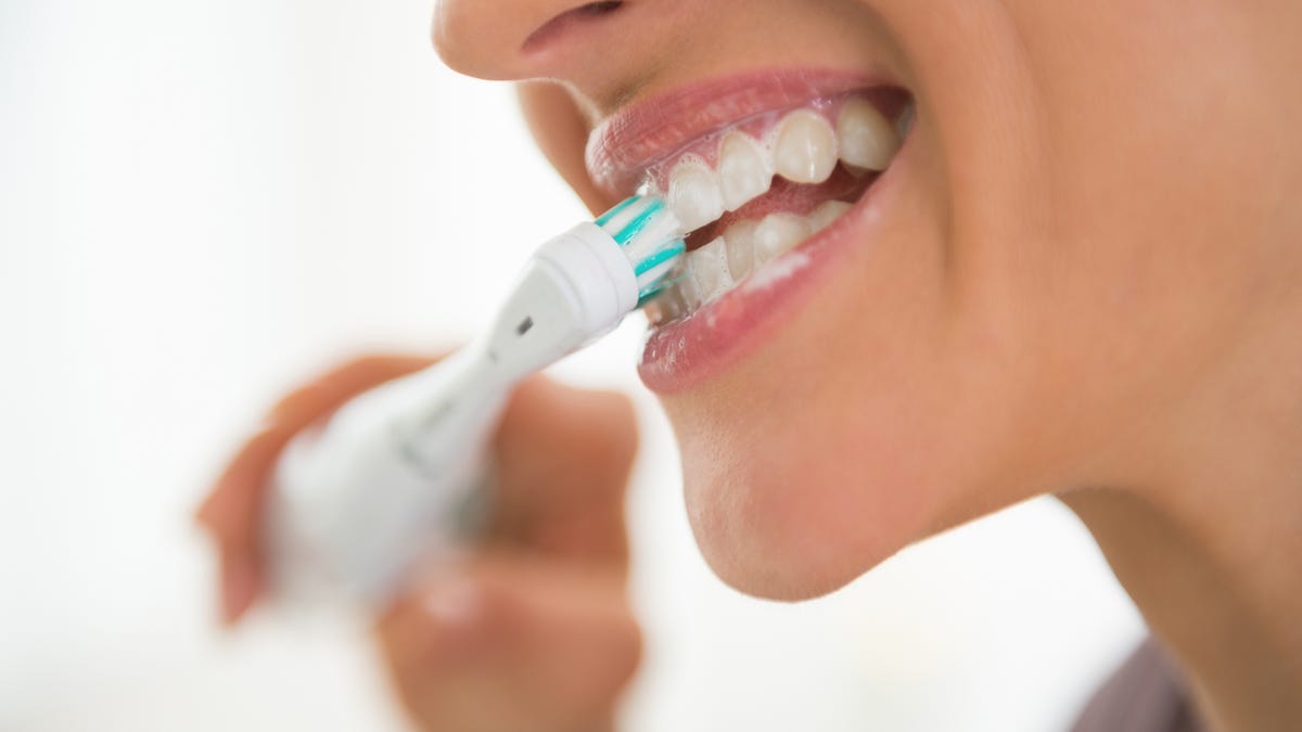 Close up of a person brushing their teeth with an electric toothbrush.