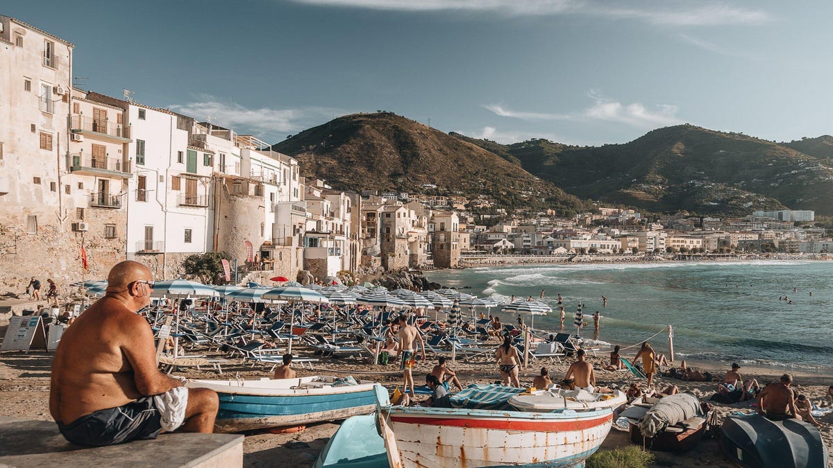 a hiker sits on a rock looking up at an outcrop and a dramatic sky