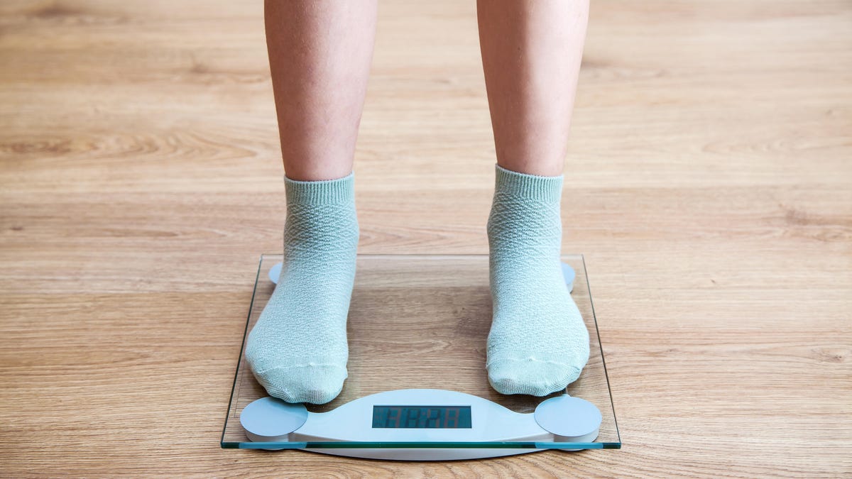 Feet with blue socks stand on a modern scale on a wood floor.