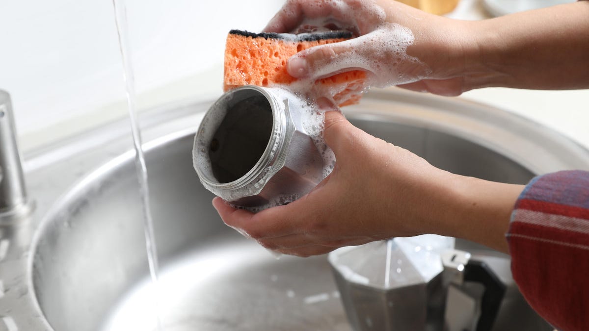 person cleaning moka pot with soap