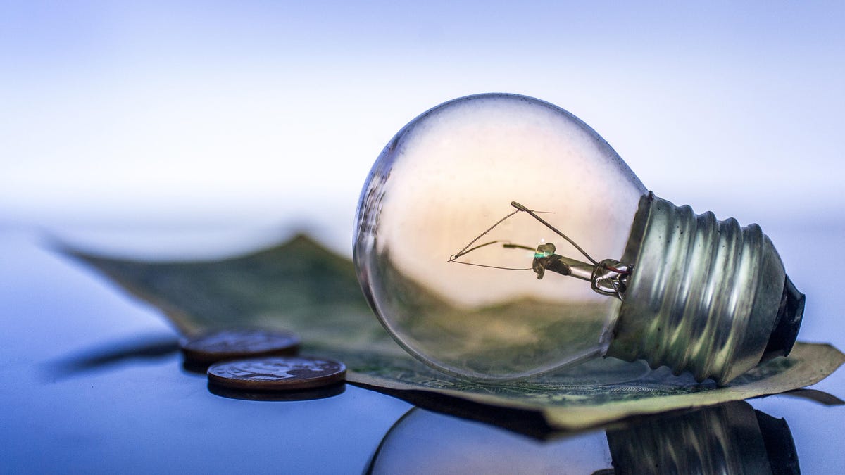 A light bulb laying on top of a dollar bill.