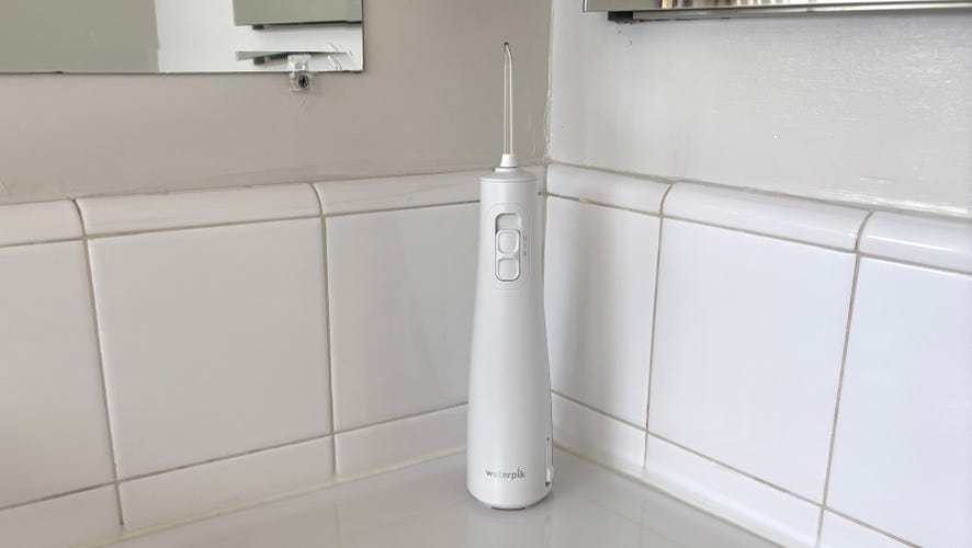 A white Waterpik Cordless Pulse 3100 water flosser on a white countertop.