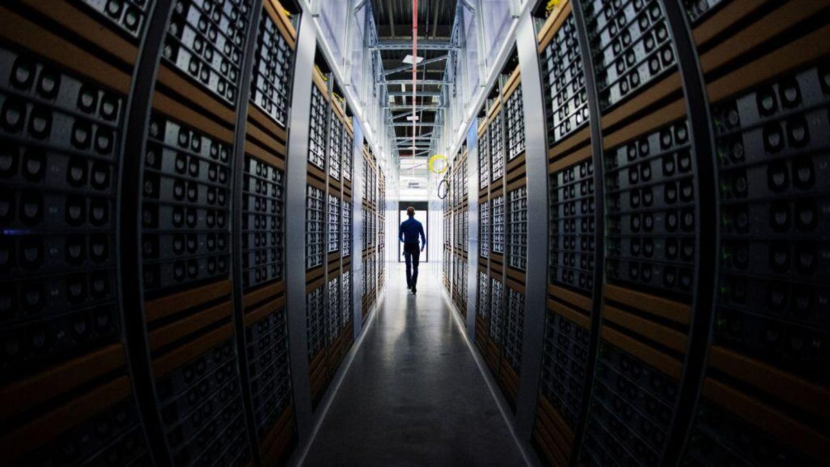 A silhouette of a person walking between two looming walls of servers in a data center