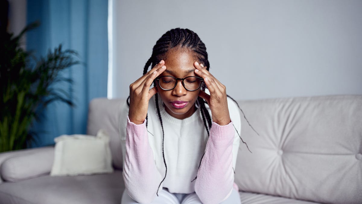 A young girl is sitting on the couch at home with her head in her hands