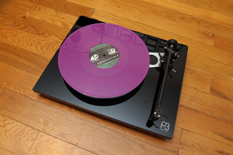 A black Rega Planar 3 turntable on a wooden background. 