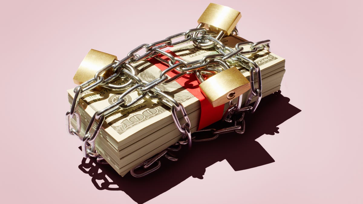 Several big stacks of $100 bills are surrounded by chains and multiple locks