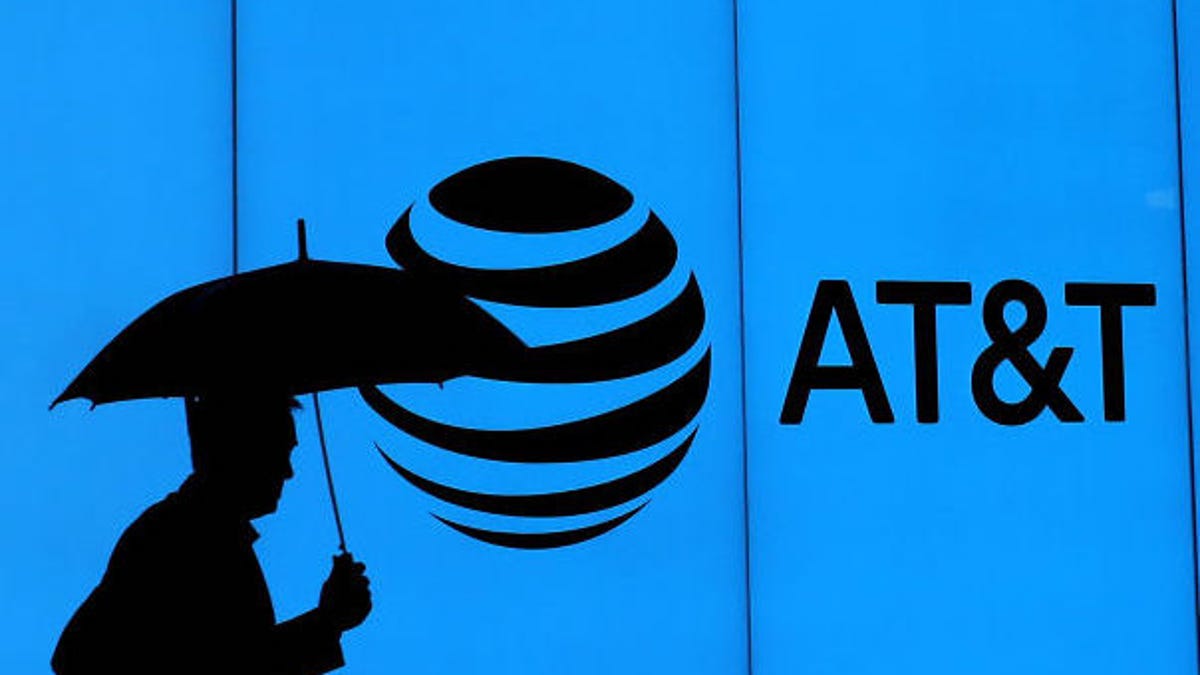 Silhouette of a man with an umbrella walking by an AT&T logo