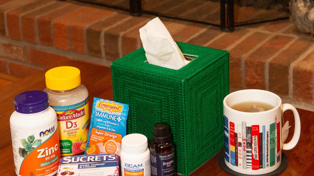 An assortment of cold treatments, a thermometer and box of tissues sitting on a table in front of a fire place.