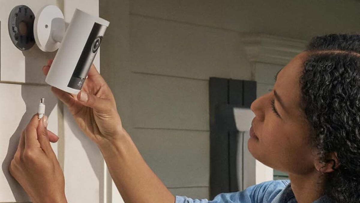 A person plugs in an outdoor Ring camera connected to exterior siding.