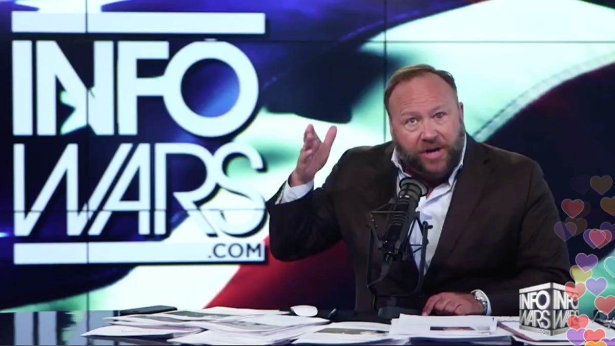 Alex Jones gestures with his hands at his broadcast desk.
