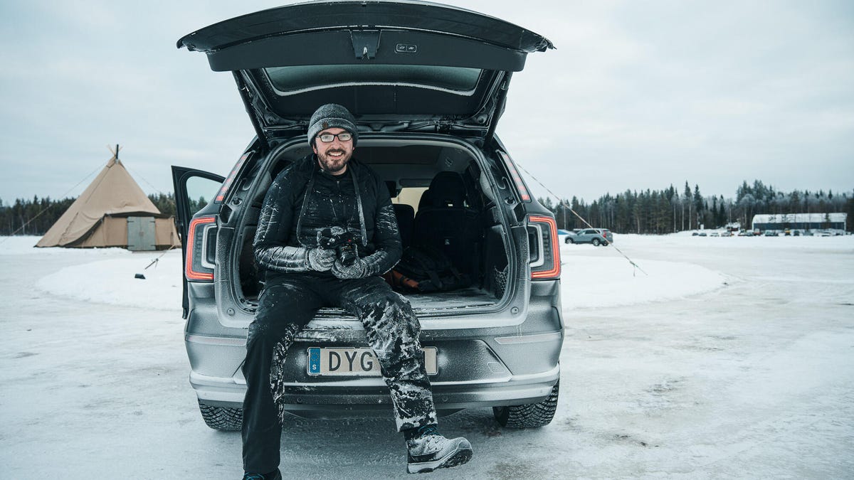 A snow-encrusted man sitting in a car's open rear hatch.