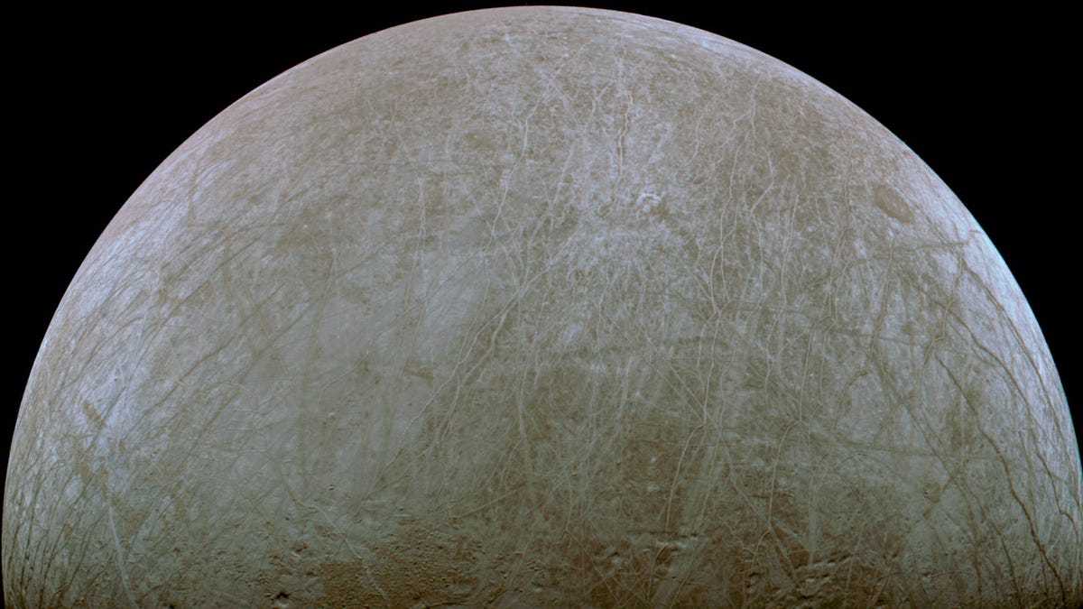 Jupiter's moon Europa shows off its icy striations and craters in a half-moon view against black.