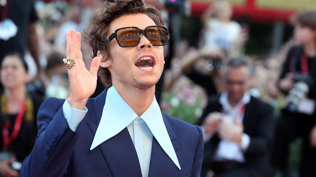 Harry Styles wearing designer sunglasses and a royal blue suit and a light blue shirt with a wildly oversize collar