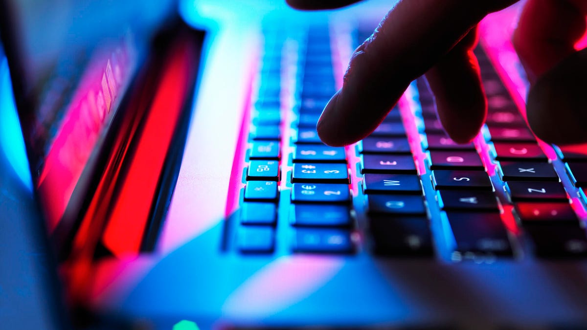 Fingers are shown typing on a keyboard lit with rainbow light