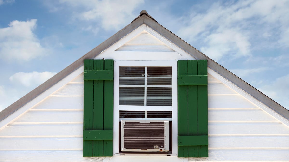 A house with upstairs window and an air conditioner mounted in it.
