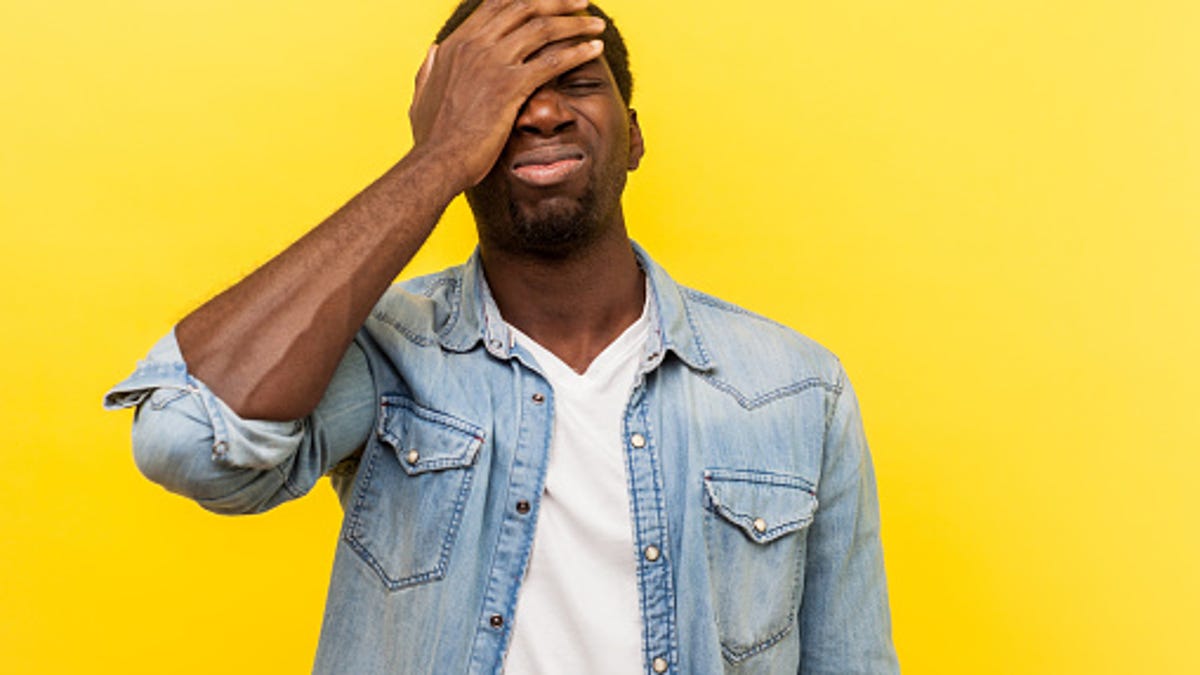 Man standing in front of a yellow background with his hand over his face.