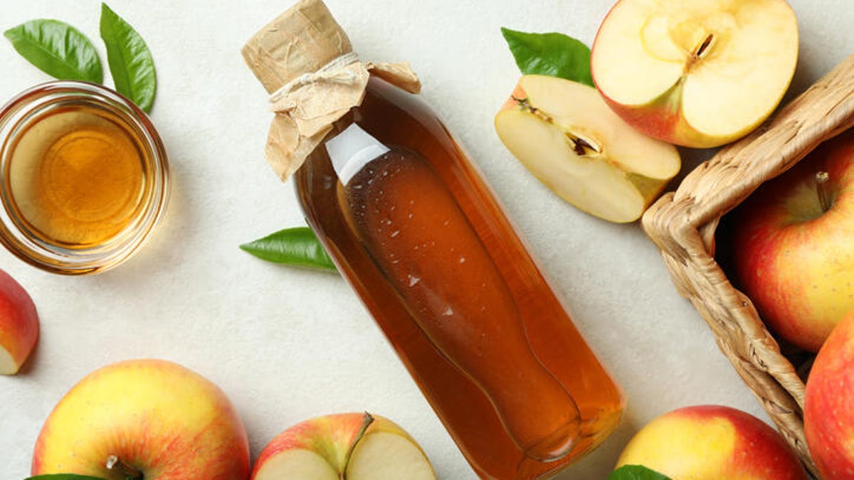 Bottle of apple cider vinegar surrounded by apples.