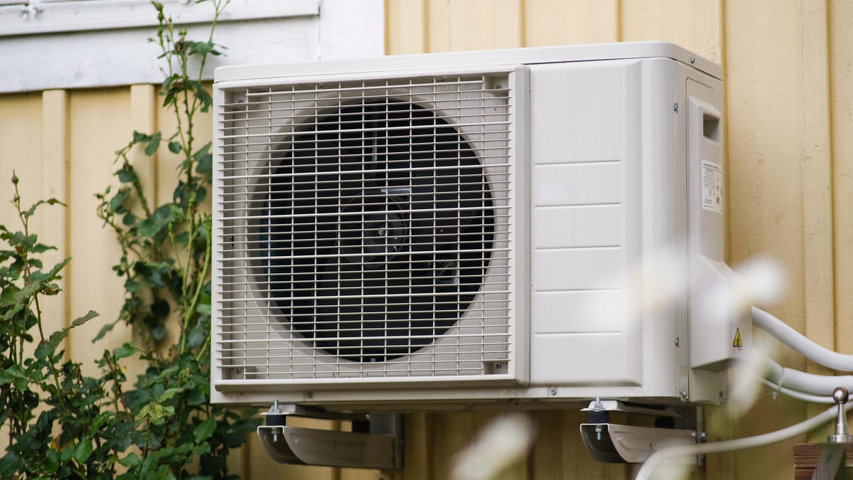A heat pump mounted on the exterior wall of a yellow house.