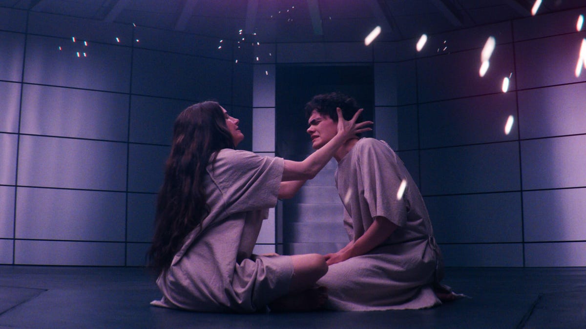 Agatha Harkness holds Billy Kaplan's head as they sit on the floor dressed in plain robes, sparks flying around them