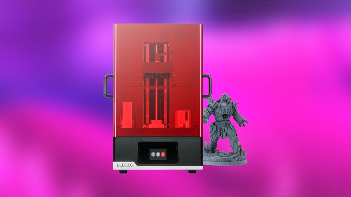 Silver-colored Elegoo 3d printer with printed cityscape against purple and orange gradient background.
