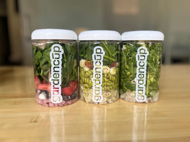 three salads in a row on a brown table in an office.