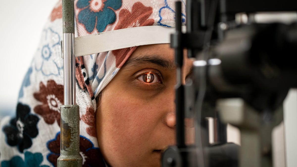A person wearing a floral hijab getting an eye exam in front of a machine with a light shining on their eye.