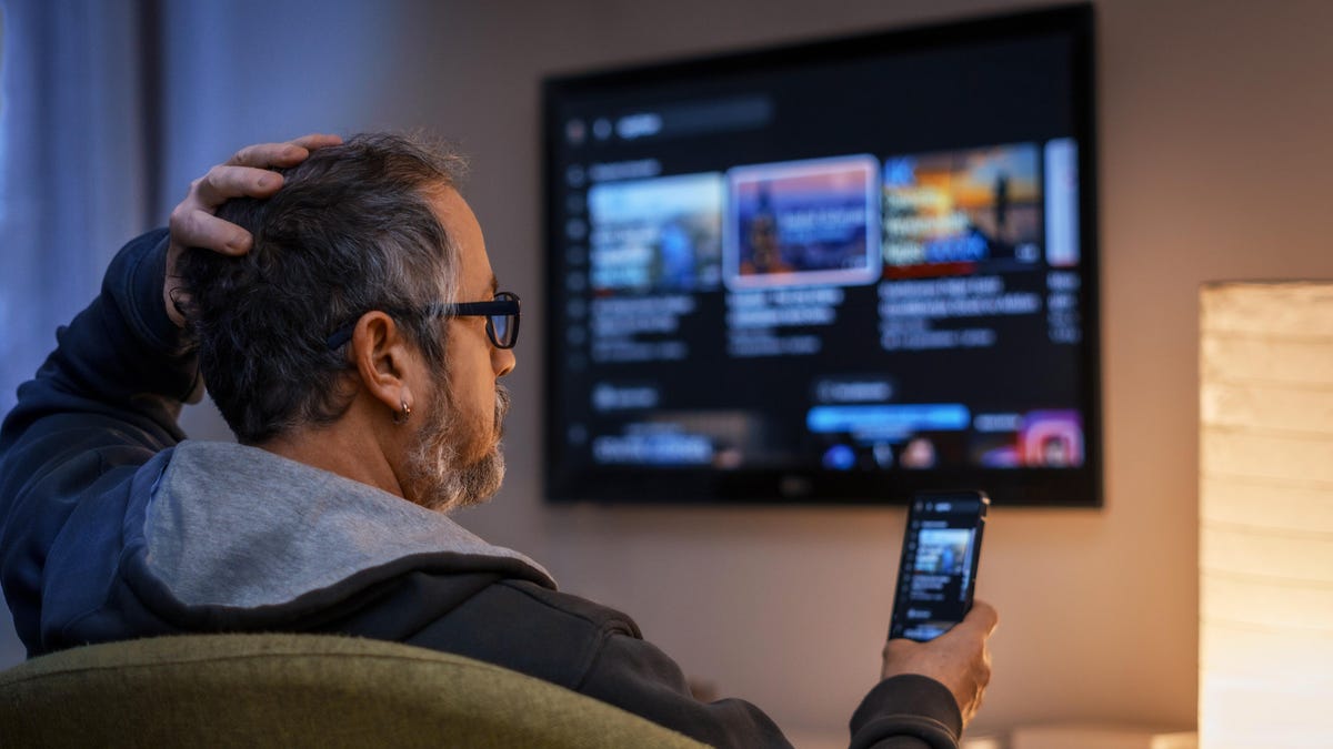 man holds a phone as he decides what to watch on TV