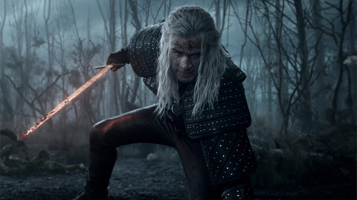 A promotional still from The Witcher Season 4 showing Liam Hemsworth scrounging down, holding a sword.
