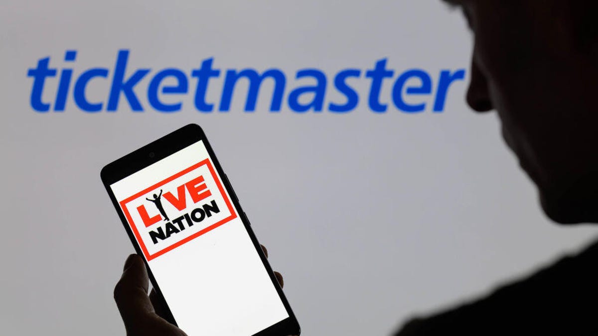 An image of a man holding a phone showing the Live Nation logo in front of the Ticketmaster logo.