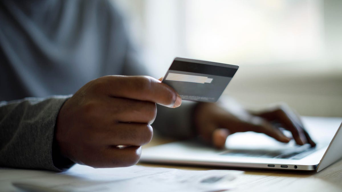 A person holds a credit card while sitting in front of a laptop computer, getting ready to make a purchase.