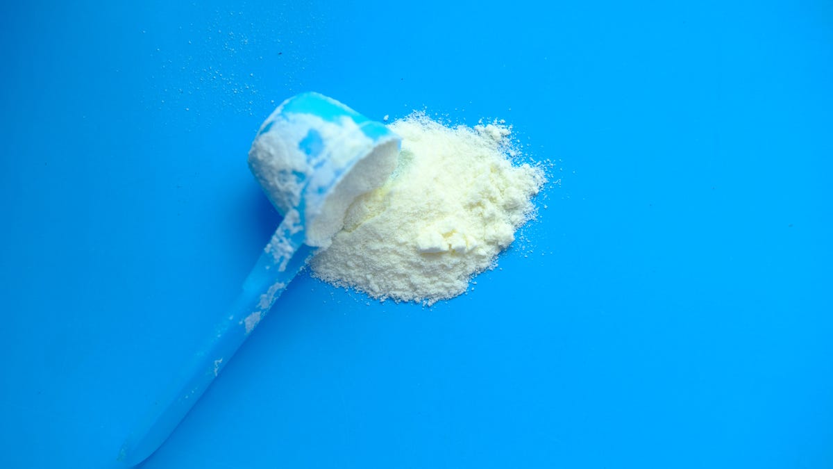 A scoop of baby formula against a bright blue background.