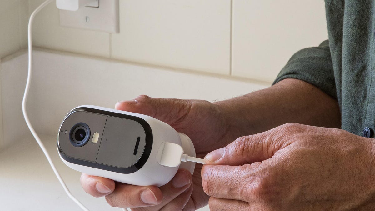 Hands plug a charging cable into a white Arlo cam.