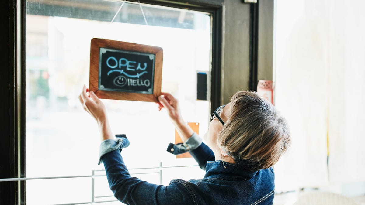 Senior female business owner turning open sign on door