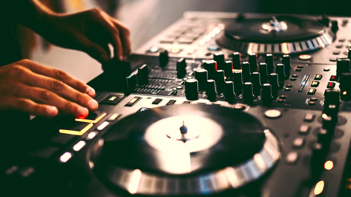 A closeup of a DJ mixing table with a DJ's hands on the controls. gettyimages-2194731676